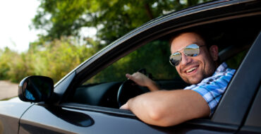 a man driving a car smiling out the window at the camera