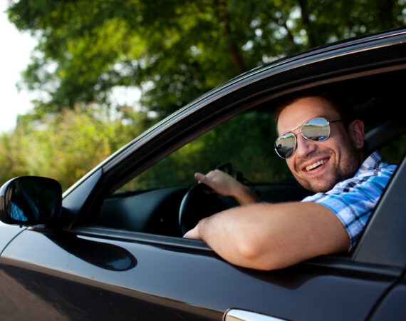 a man driving a car smiling out the window at the camera