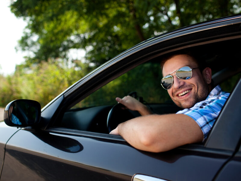 a man driving a car smiling out the window at the camera