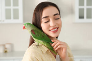 a woman with a green bird on her shoulder who she's stroking lovingly