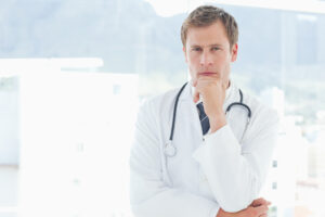 a white man in a lab coat with a stethoscope is stroking his chin in thought