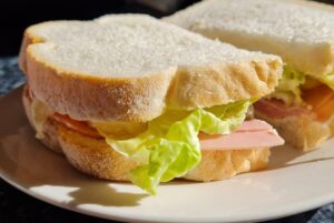 ham sandwich, made with white bread and lettuce, on a white plate.