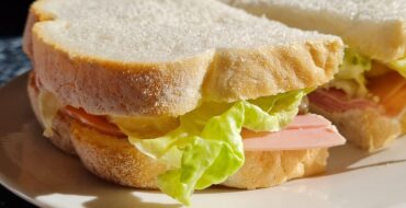 ham sandwich, made with white bread and lettuce, on a white plate.