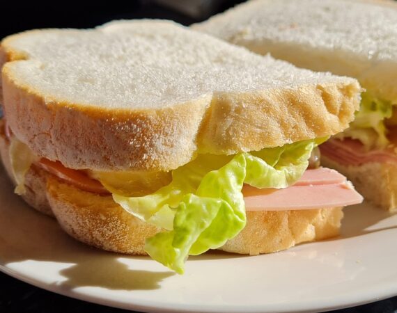 ham sandwich, made with white bread and lettuce, on a white plate.