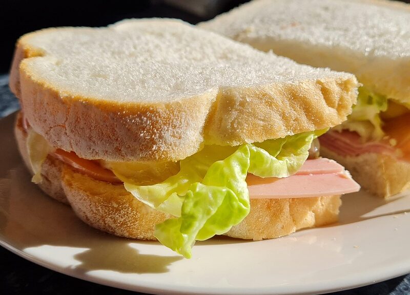 ham sandwich, made with white bread and lettuce, on a white plate.