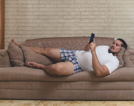 A typical couch potato - A man in his underwear laying on the sofa and watching videos, playing mobile games or on social media.