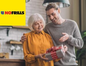 A young man is happily giving his mother a nicely wrapped gift. There's a yellow "No Frills" logo in the upper left corner.