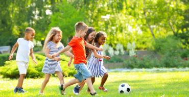 a group of five young children playing soccer on a green lawn on a beautiful day