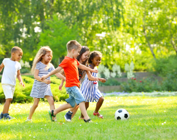 a group of five young children playing soccer on a green lawn on a beautiful day