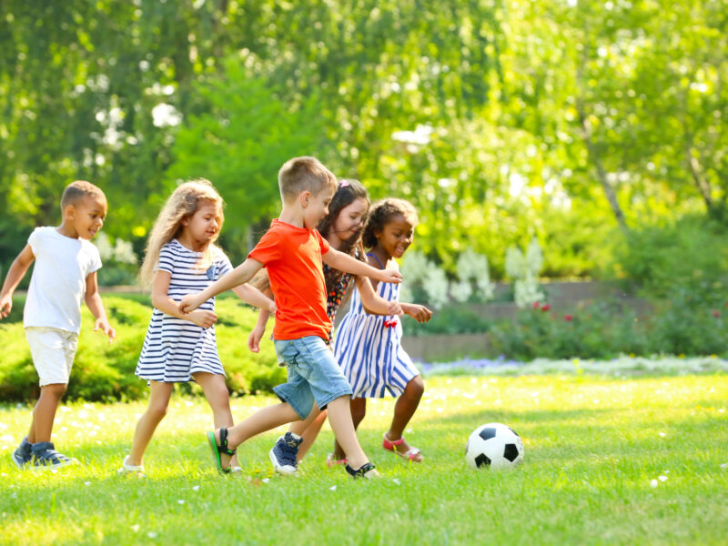 a group of five young children playing soccer on a green lawn on a beautiful day