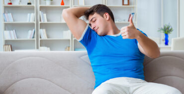 A man is sitting down, smelling his own sweaty armpit and giving a thumbs up