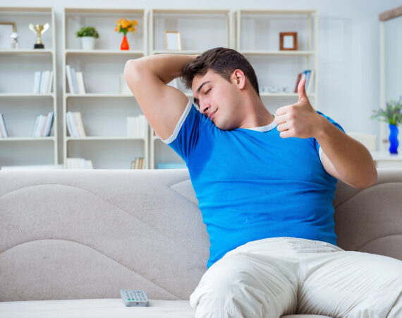 A man is sitting down, smelling his own sweaty armpit and giving a thumbs up