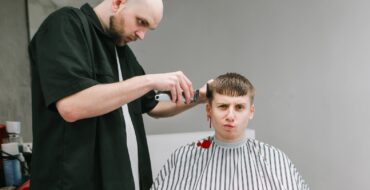 A man getting a haircut with an unhappy expression on his face while his right ear bleeds