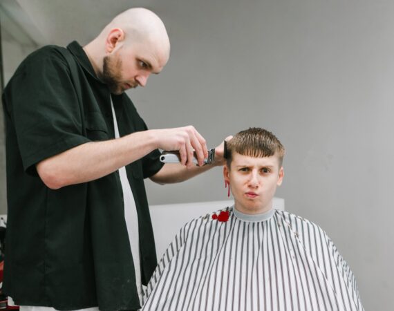 A man getting a haircut with an unhappy expression on his face while his right ear bleeds