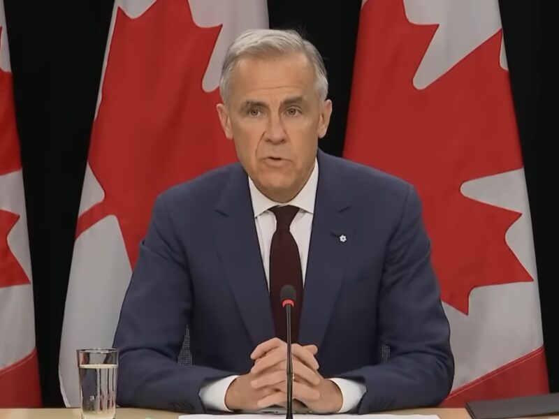 Mark Carney sitting at a desk in front of several Canadian flags