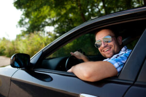 a man driving a car smiling out the window at the camera