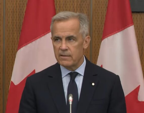 Mark Carney giving a speech in front of Canadian flags